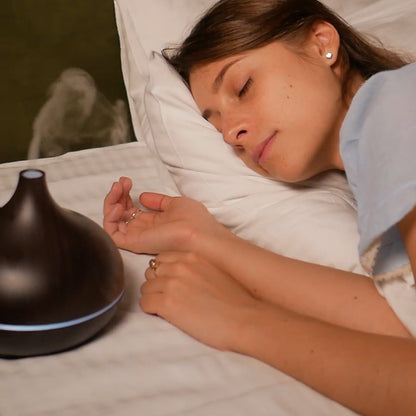 Dark wood-grain diffuser on a bed beside a sleeping woman